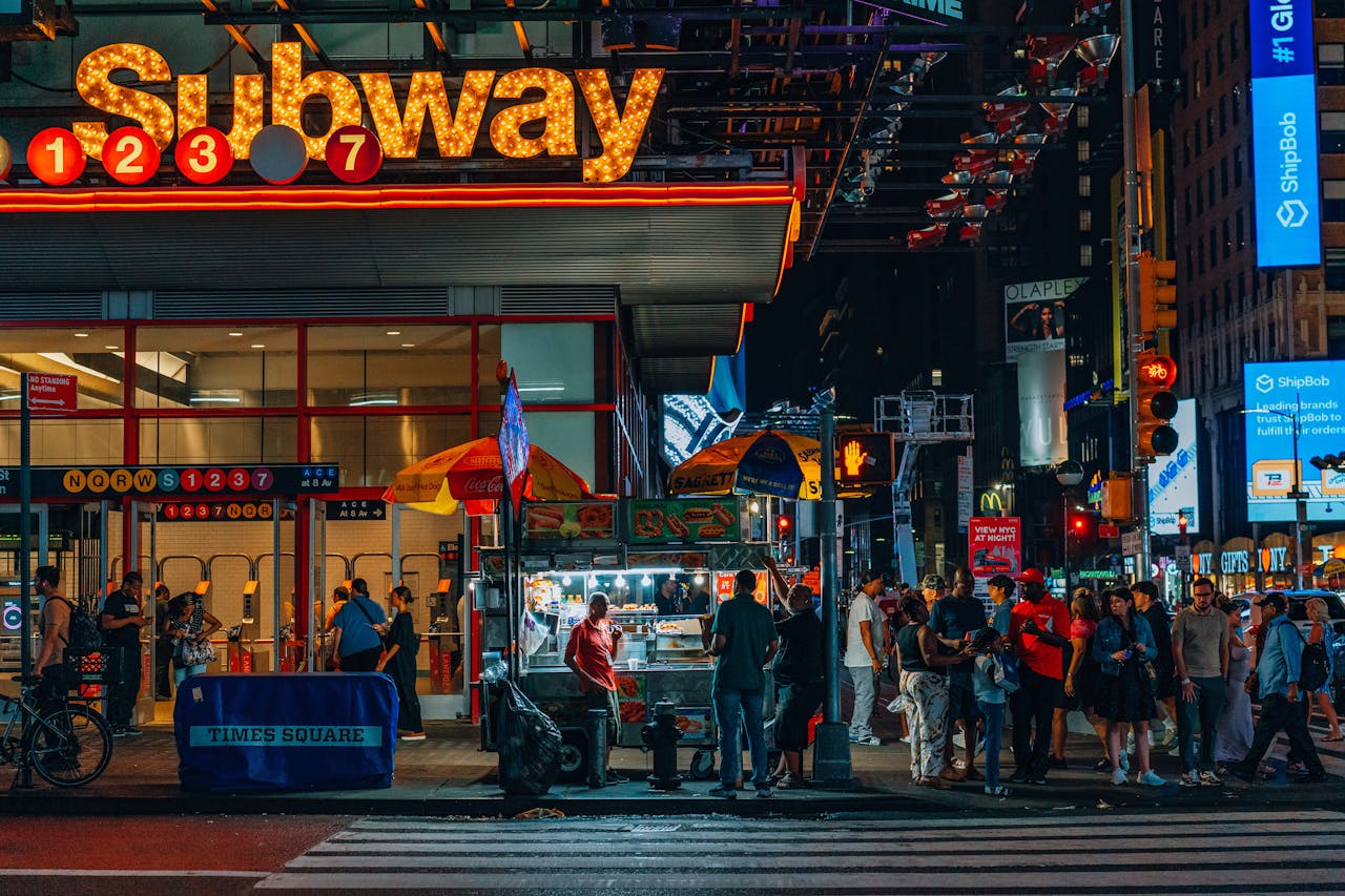 Crowds enjoying the energetic nightlife at a Times Square subway entrance, under bright neon lights.