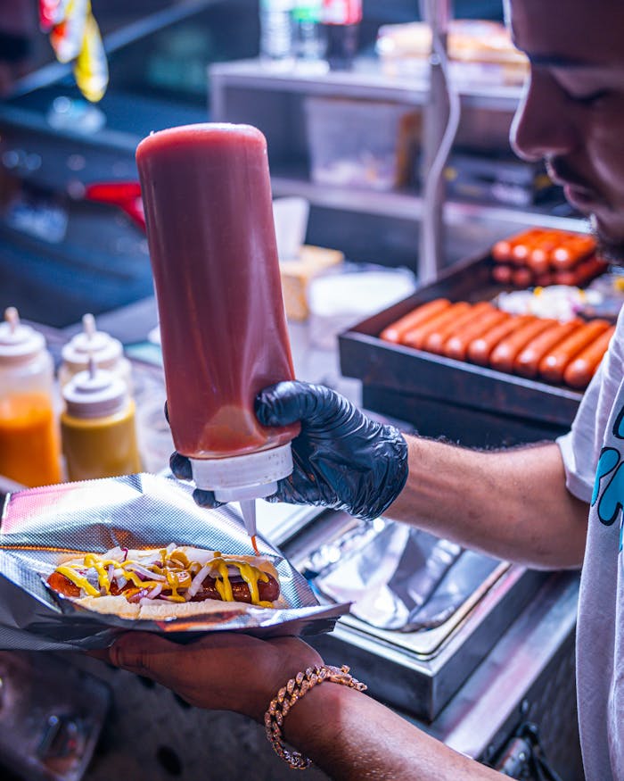 Services Street food vendor adds ketchup and mustard to a hot dog in Nashville, TN at night.