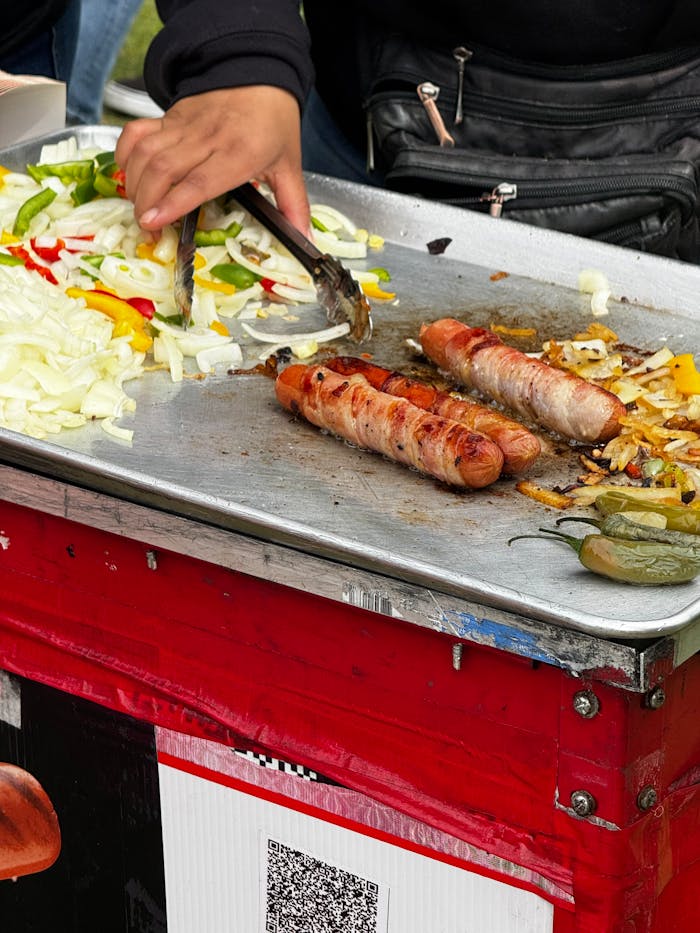 Services Vibrant street scene of a vendor grilling bacon-wrapped sausages with vegetables.